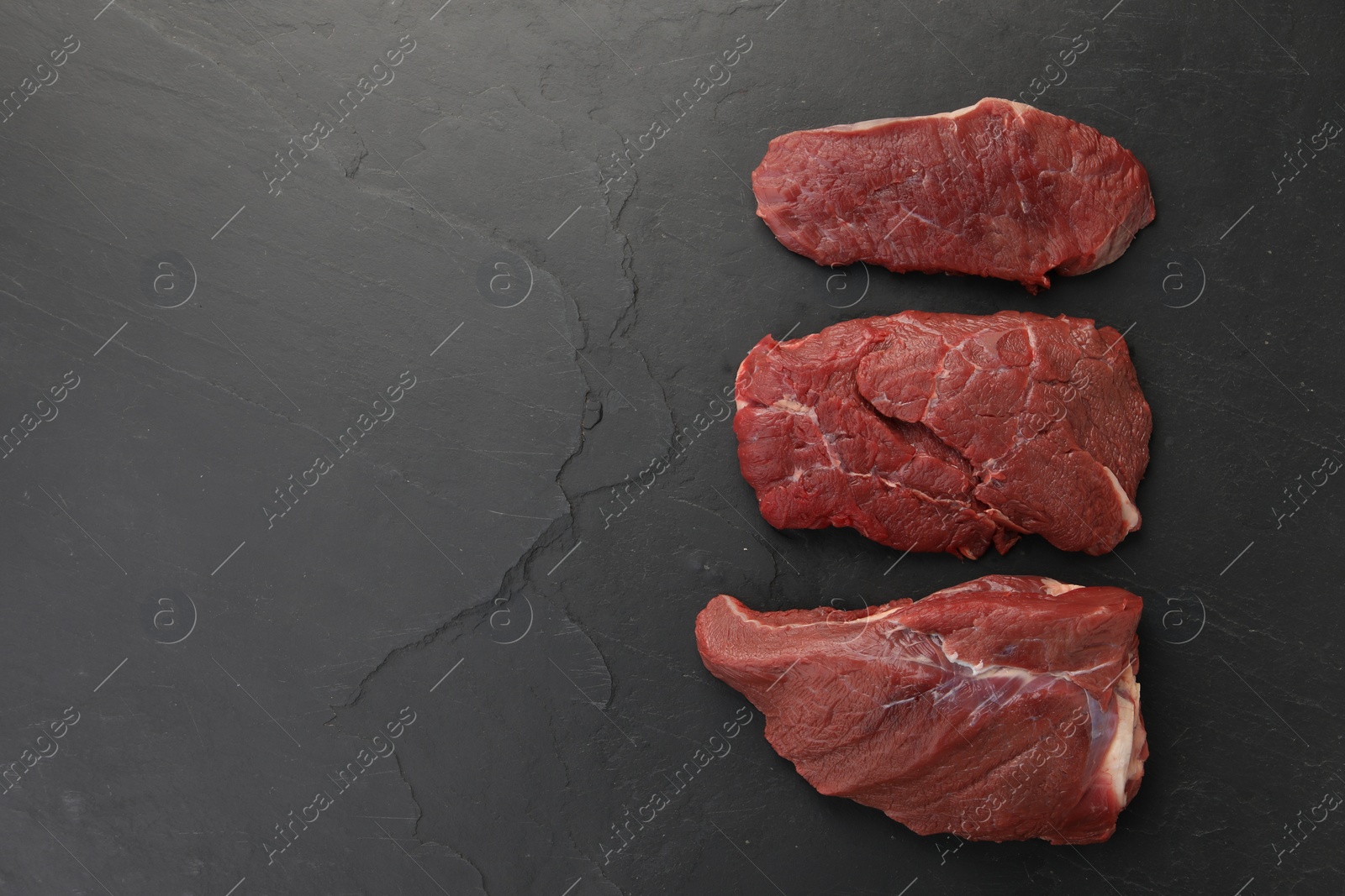 Photo of Pieces of raw beef meat on black table, flat lay. Space for text