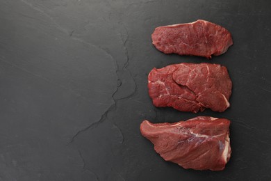 Photo of Pieces of raw beef meat on black table, flat lay. Space for text