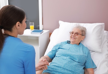 Nurse assisting senior woman lying on bed in hospital ward