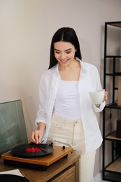 Photo of Happy young woman using turntable at home