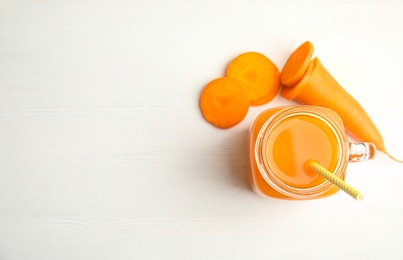 Photo of Freshly made carrot juice in mason jar on white wooden table, flat lay. Space for text