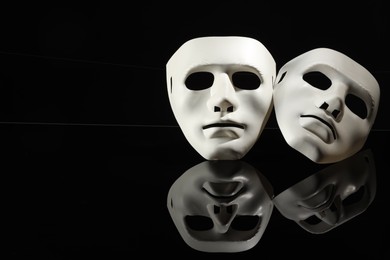 Photo of Plastic face masks on black mirror surface, space for text. Theatrical performance