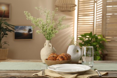 Photo of Clean tableware, flowers and fresh pastries on table in stylish dining room
