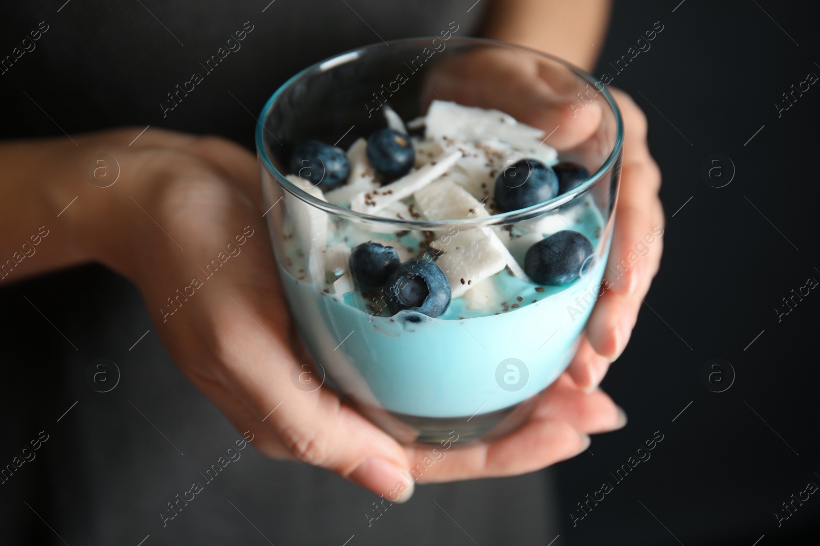 Photo of Woman holding glass cup of spirulina smoothie on dark background, closeup