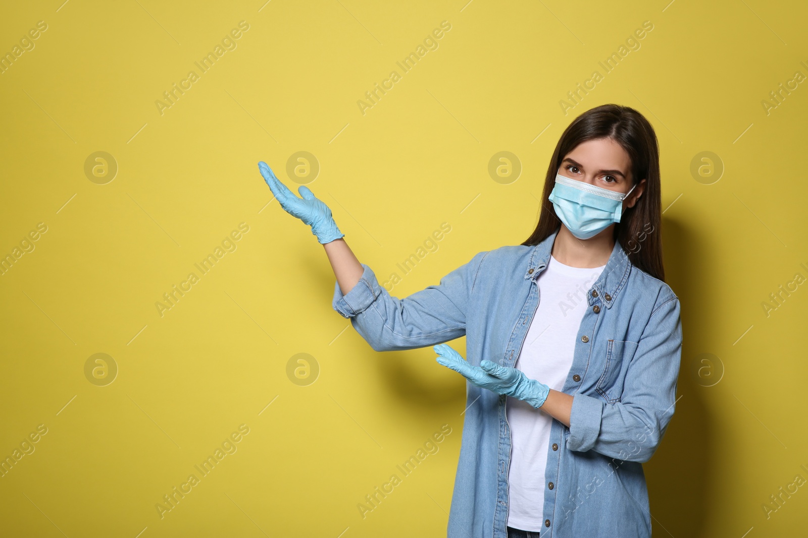 Photo of Female volunteer in mask and gloves on yellow background, space for text. Protective measures during coronavirus quarantine