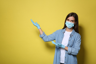 Photo of Female volunteer in mask and gloves on yellow background, space for text. Protective measures during coronavirus quarantine