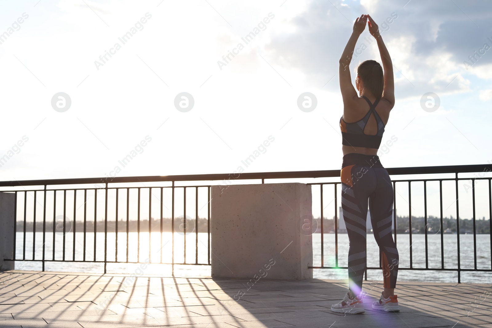 Photo of Young woman stretching on pier near river in morning, back view. Space for text