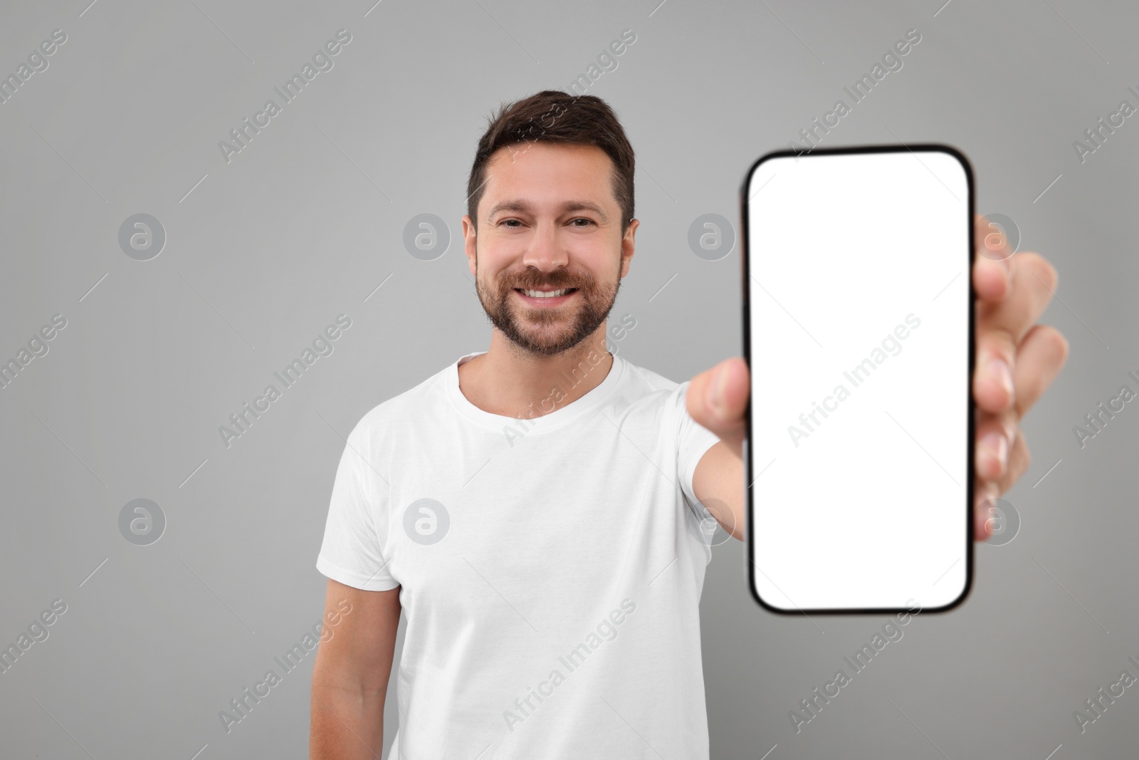 Photo of Handsome man showing smartphone in hand on light grey background