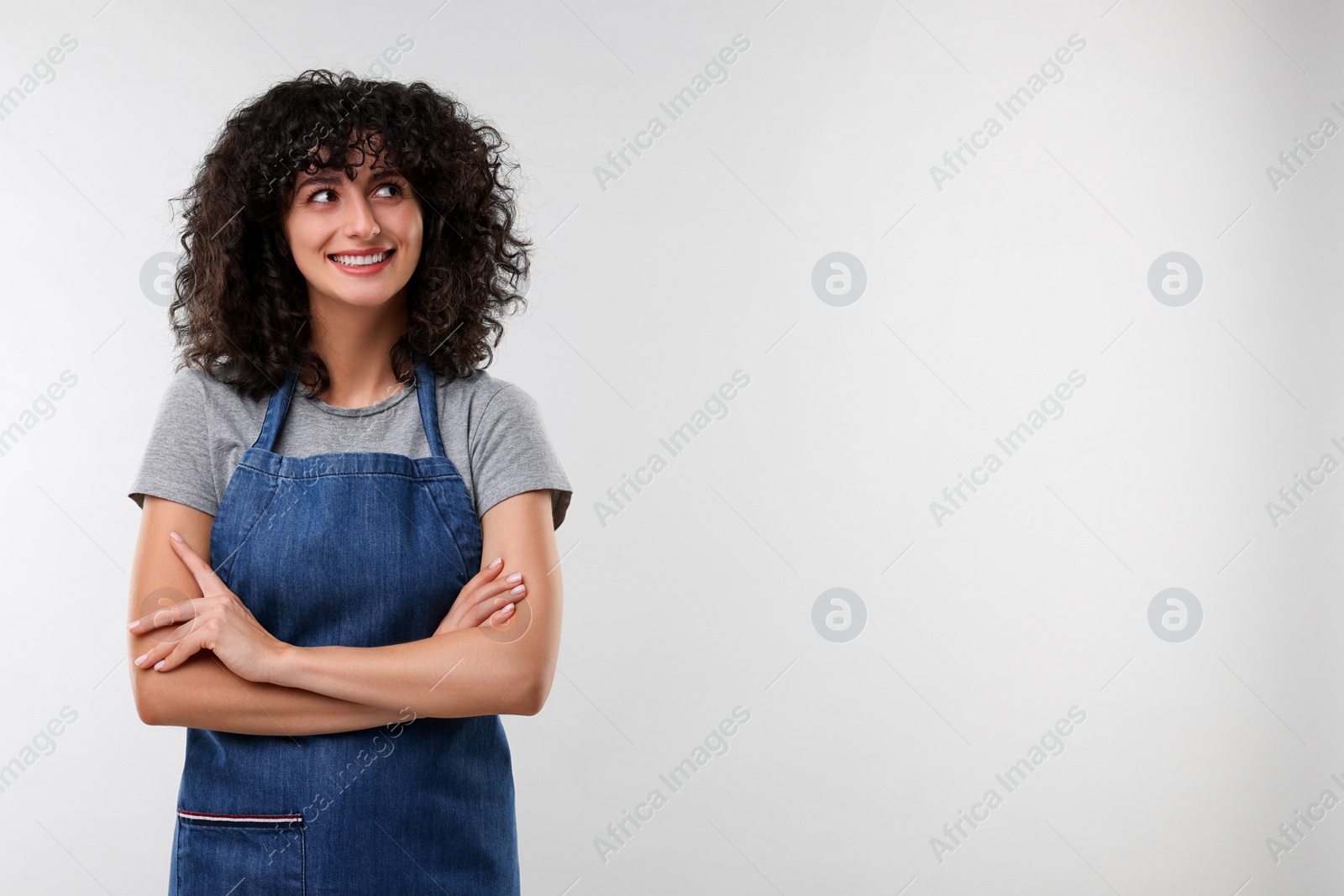 Photo of Happy woman wearing kitchen apron on light grey background, space for text. Mockup for design