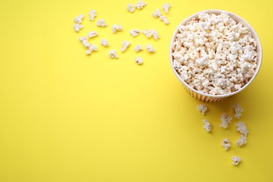 Photo of Paper bucket with delicious popcorn on yellow background, flat lay. Space for text