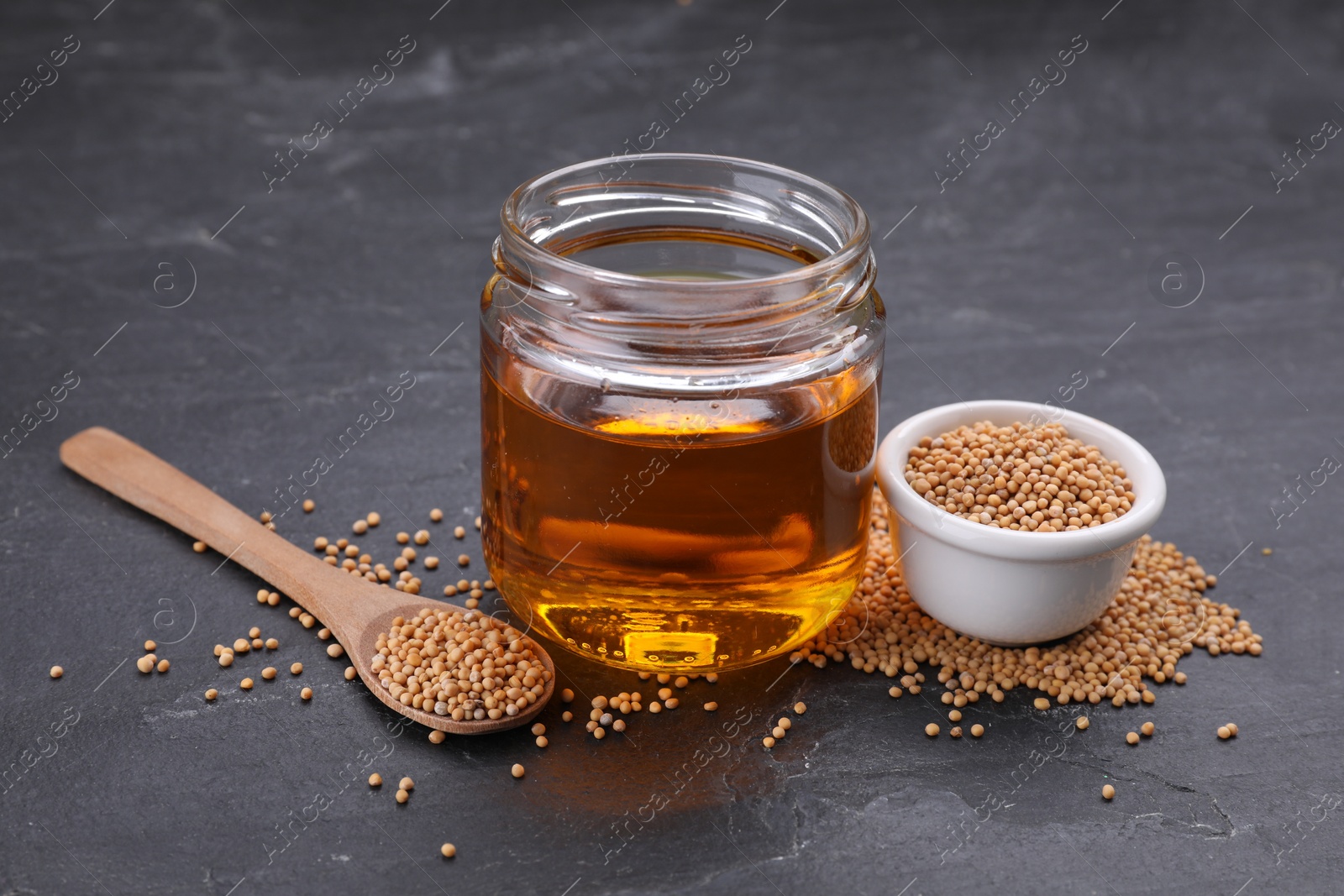 Jar with natural oil and mustard seeds on black table Photo of Jar with natural oil and mustard seeds on black table