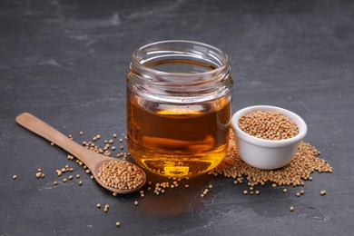 Photo of Jar with natural oil and mustard seeds on black table
