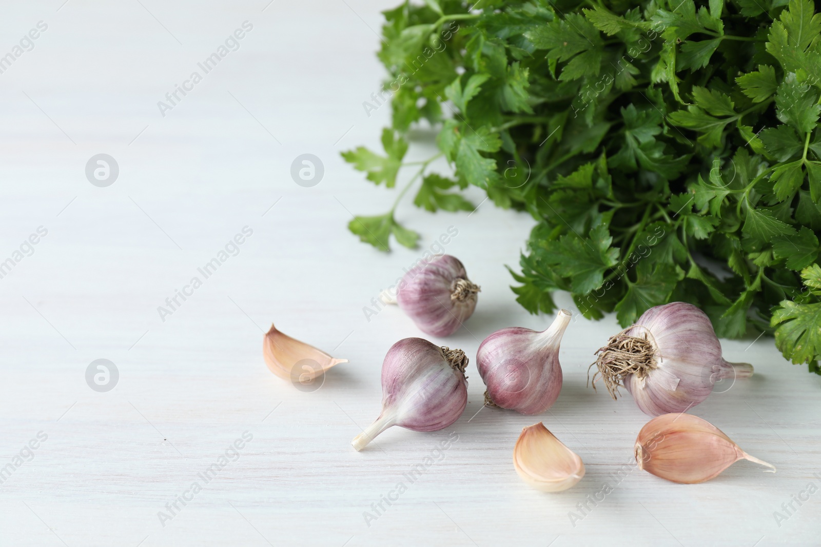 Photo of Fresh raw garlic and parsley on white wooden table, space for text