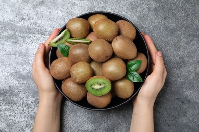 Photo of Woman holding bowl with fresh ripe kiwis at grey table, top view