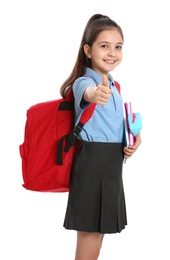 Photo of Cute little girl in school uniform with backpack and stationery showing thumbs-up on white background
