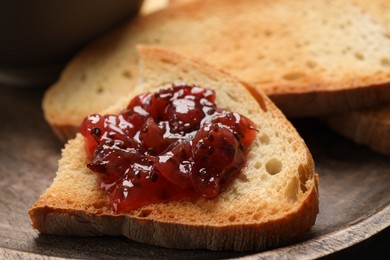 Slice of toasted bread with gooseberry jam on wooden plate, closeup