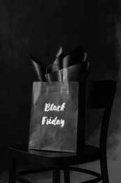 Photo of Shopping bag with words Black Friday on chair against dark background