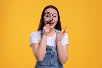Photo of Happy young woman looking through magnifier glass on yellow background