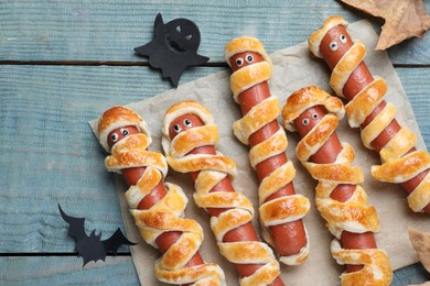Photo of Cute sausage mummies served on blue wooden table, flat lay. Halloween party food