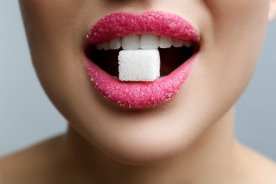 Woman with beautiful lips eating sugar cube on light grey background, closeup