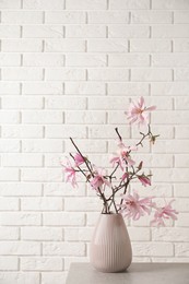 Magnolia tree branches with beautiful flowers in vase on grey table against white brick wall