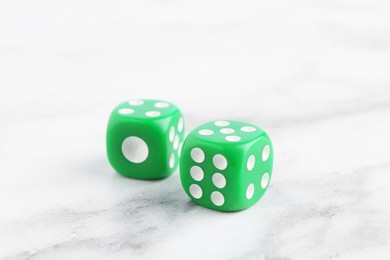 Photo of Two green game dices on white marble table, closeup