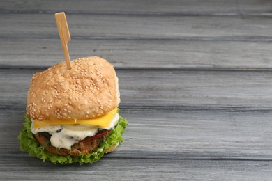 Photo of Delicious vegetarian burger on grey wooden table, space for text