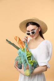 Photo of Woman with string bag of fresh vegetables and baguette on beige background
