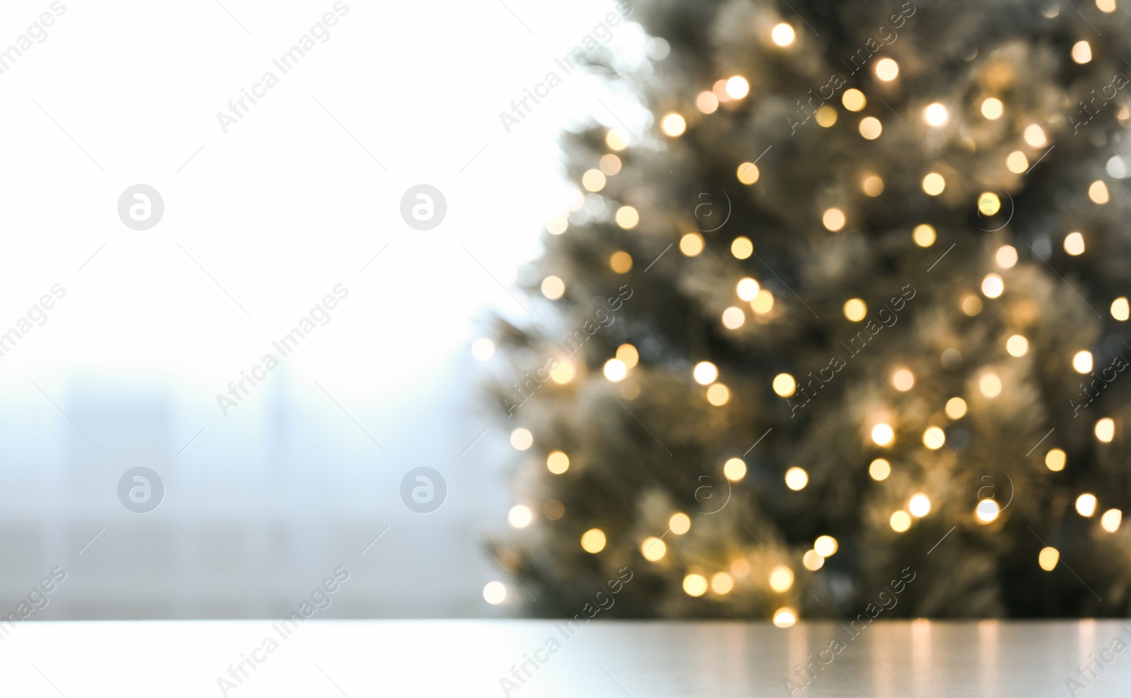 Photo of Blurred view of beautiful Christmas tree with yellow lights near window indoors, focus on table. Space for text