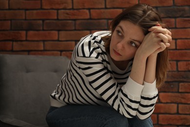 Photo of Sad young woman sitting on chair near brick wall