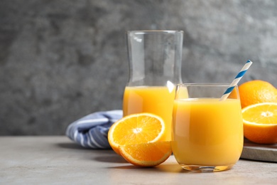 Photo of Glass of orange juice and fresh fruits on grey table. Space for text