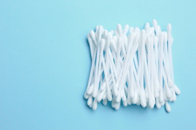 Photo of Heap of cotton buds on light blue background, top view. Space for text