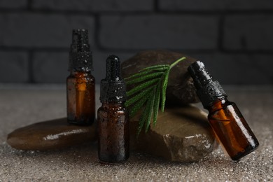 Photo of Bottles of organic cosmetic products, green leaf and stones on wet surface