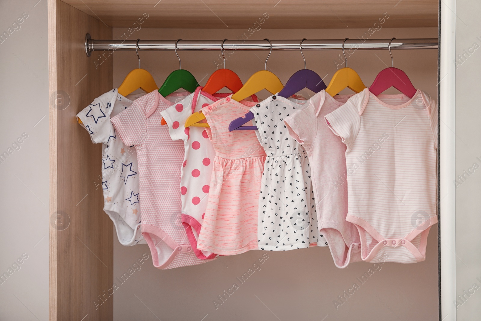 Photo of Hangers with baby clothes on rack in wardrobe