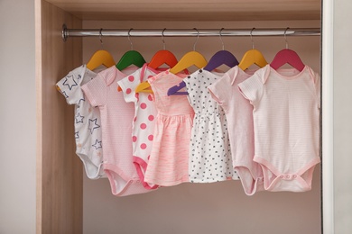 Photo of Hangers with baby clothes on rack in wardrobe