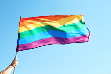 Gay man holding rainbow LGBT flag on blue sky background