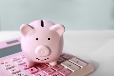 Photo of Ceramic piggy bank and calculator on white marble table, closeup. Space for text