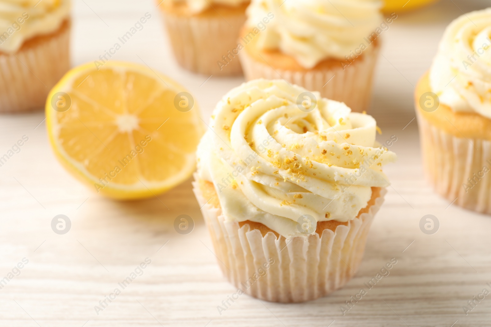 Photo of Tasty cupcakes with cream, lemon zest and fruit on white wooden table, closeup