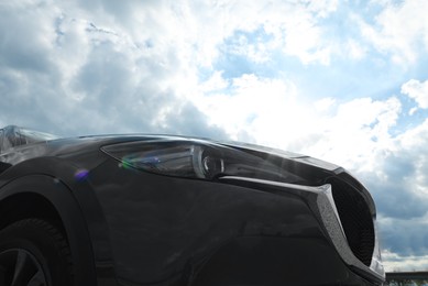 Photo of New black modern car against cloudy sky, closeup of headlight
