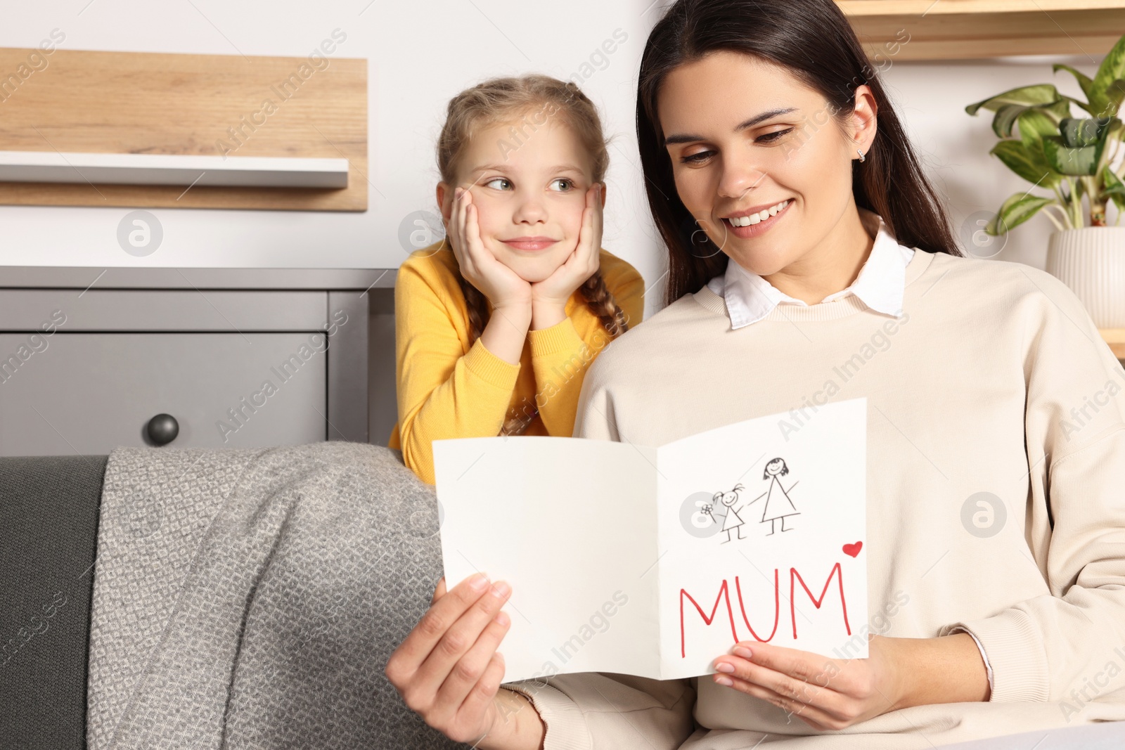 Photo of Happy woman receiving greeting card from her little daughter at home