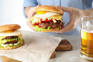 Woman holding tasty burger with fried egg over table, closeup