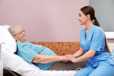 Photo of Nurse assisting senior woman lying on bed in hospital ward