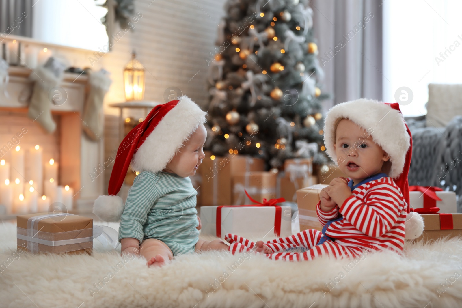 Image of Cute children in Santa hats on floor in room with Christmas tree