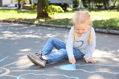 Photo of Little child drawing with colorful chalk on asphalt