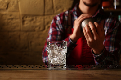 Bartender preparing fresh alcoholic cocktail at bar counter, focus on glass