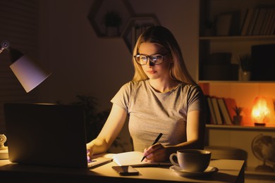 Home workplace. Woman with pen and notebook working on laptop at white desk in room