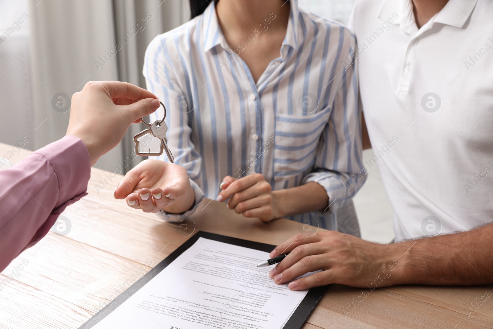 Photo of Real estate agent giving house key to couple at table in office, closeup