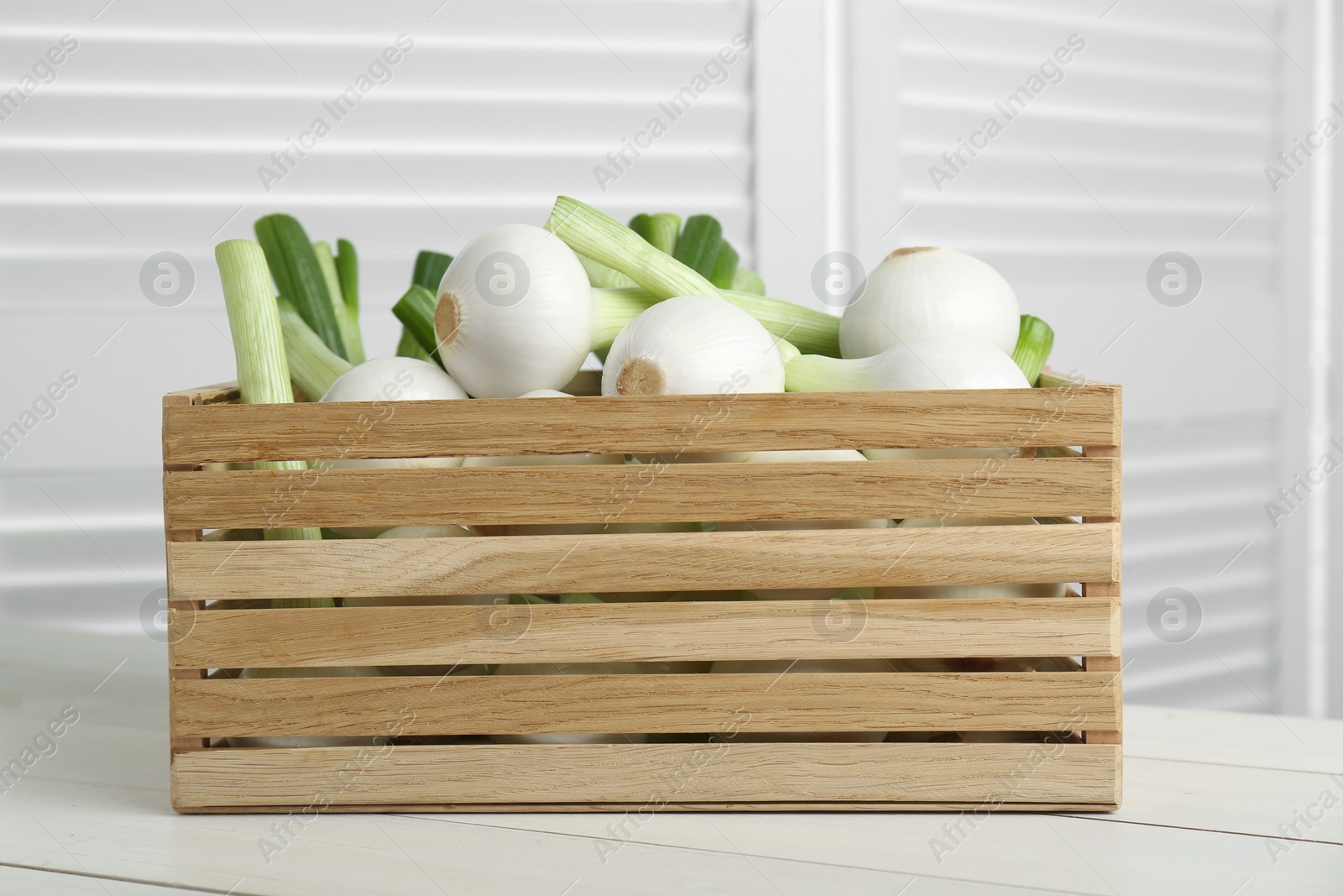 Photo of Crate with green spring onions on white wooden table