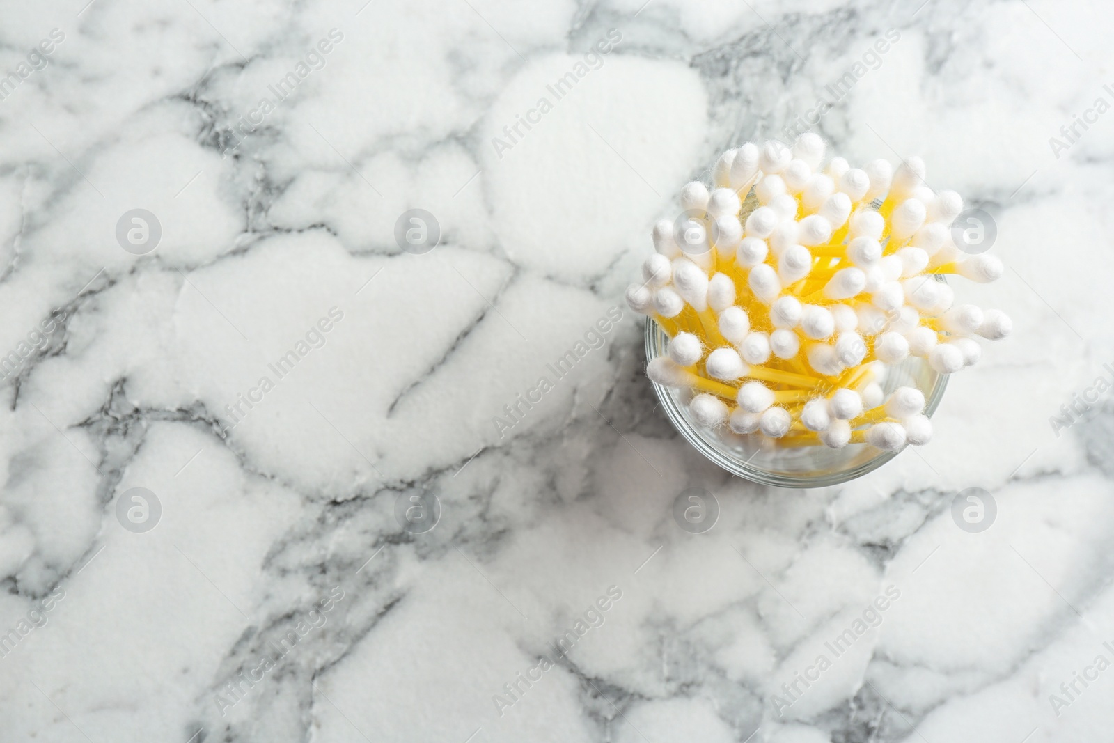 Photo of Glass with cotton swabs on marble background, top view. Space for text