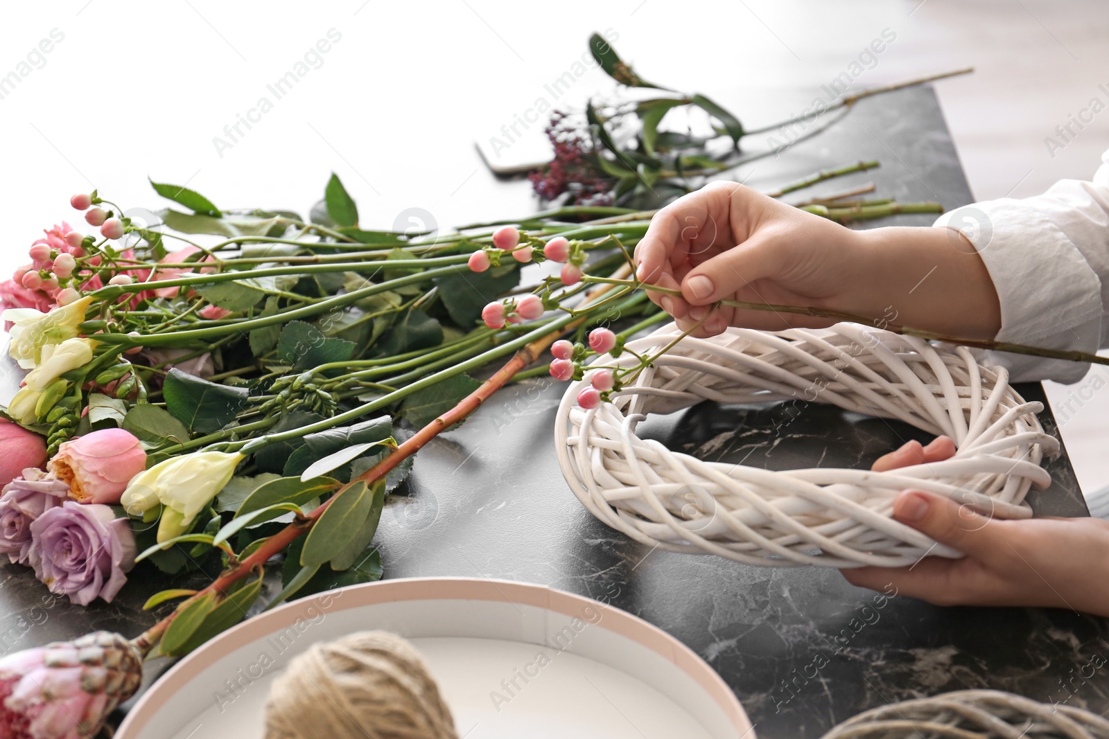 Photo of Female florist creating beautiful wreath at table, closeup
